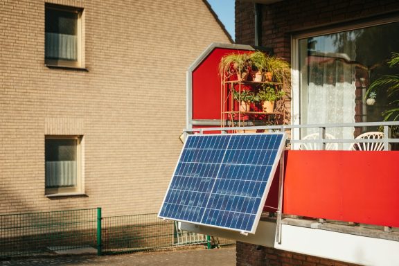 Wirtschaftlichkeit Solarmodul an einem Balkon mit roten Wänden und blühenden Pflanzen.