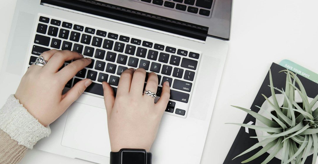 Hände tippen auf einer Laptop-Tastatur neben einem Pflanzentopf und Notizen.